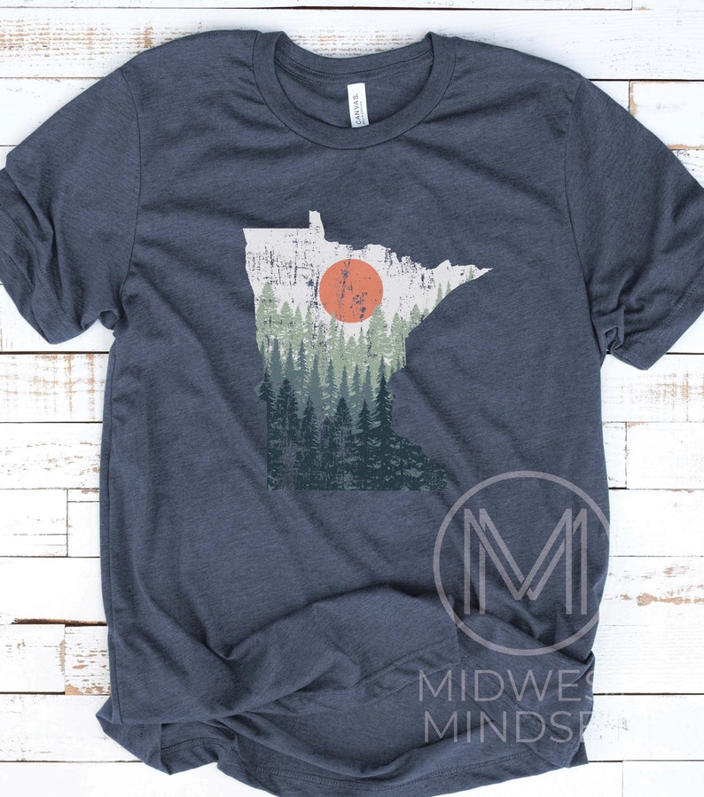 May include: A navy blue t-shirt with a vintage-style graphic of the state of Minnesota. The graphic features a forest scene with a large orange sun in the background.