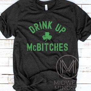 May include: A dark grey t-shirt with a green shamrock and the text "Drink Up McBitches" in a distressed font.