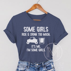 May include: A navy blue t-shirt with white text that reads "Some girls ride & drink too much. It's me. I'm some girls." The shirt features a white silhouette of an ATV and a shot glass.
