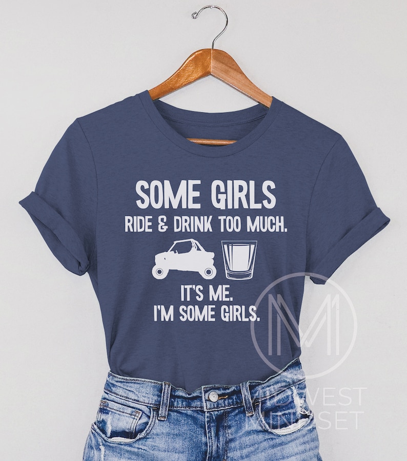 May include: A navy blue t-shirt with white text that reads "Some girls ride & drink too much. It's me. I'm some girls." The shirt features a white silhouette of an ATV and a shot glass.