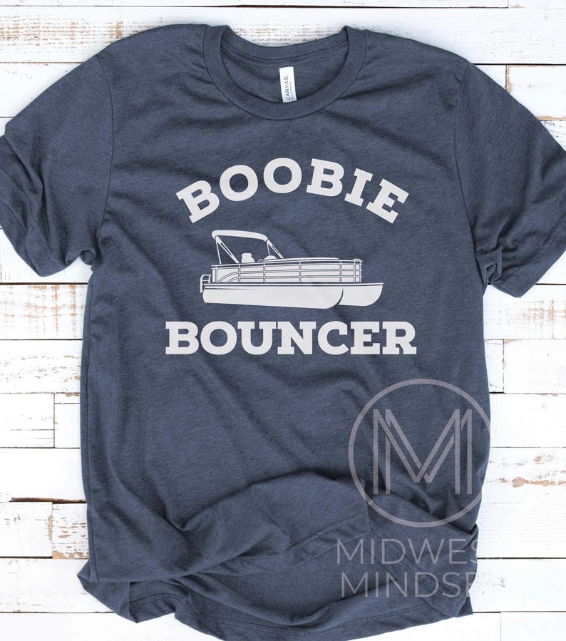 May include: A navy blue t-shirt with white text that reads "Boobie Bouncer" and a white silhouette of a pontoon boat. The shirt is made of a soft, comfortable material.