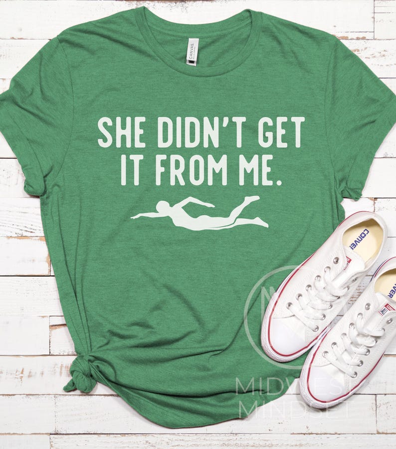 May include: Green t-shirt with the text "She didn't get it from me." and a white silhouette of a swimmer.
