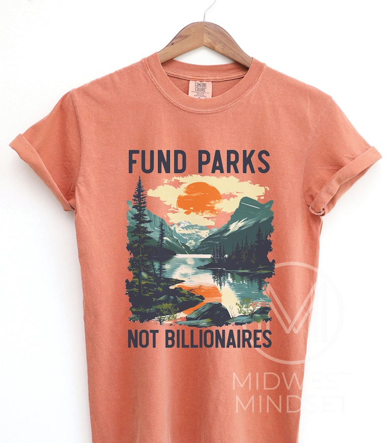 May include: A burnt orange t-shirt with a graphic of a mountain lake scene and the text "Fund Parks Not Billionaires".