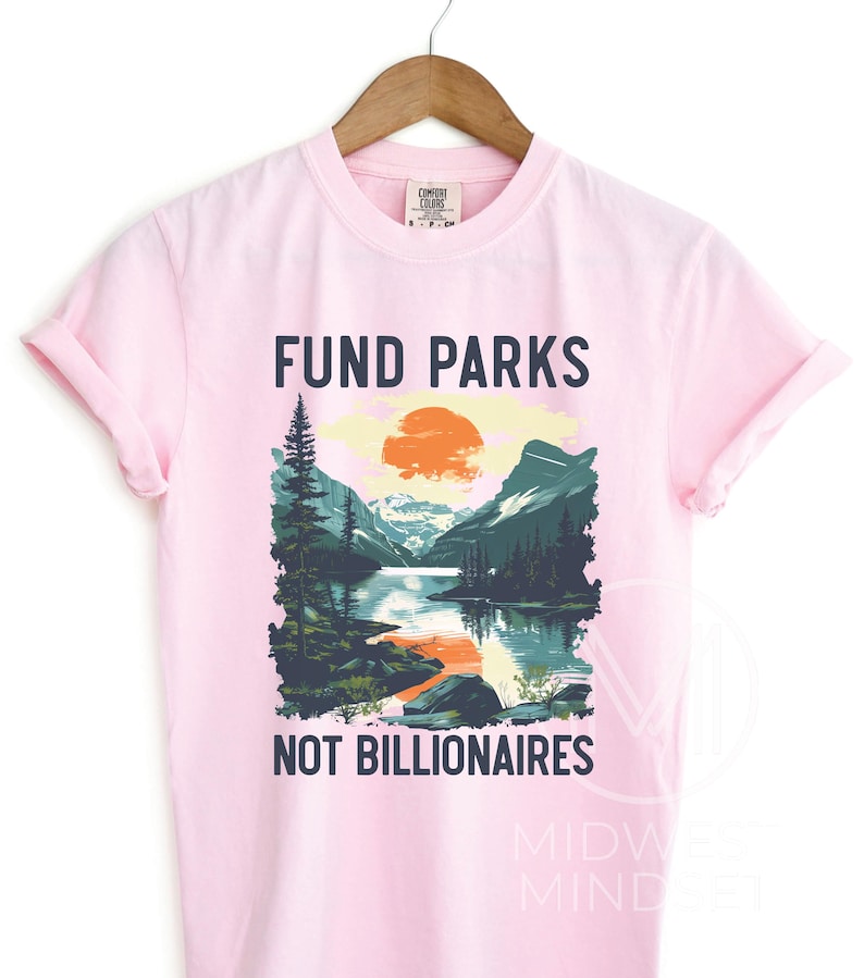 May include: Pink t-shirt with a graphic of a mountain landscape and a sunset. The text "Fund Parks Not Billionaires" is printed on the shirt.