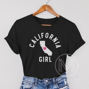 Pu&ograve; includere: Maglietta nera con un contorno bianco dello stato della California e le parole "California Girl" con un cuore rosa all'interno del contorno dello stato.