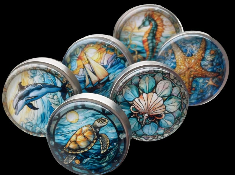 May include: Six round, silver-toned cabinet knobs with colourful, ocean-themed images. The images include a dolphin, a sailboat, a seashell, a starfish, a seahorse, and a sea turtle.