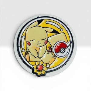 May include: A circular enamel pin featuring a yellow Pikachu character with closed eyes, sleeping inside a yellow frame. The design includes a red and white Poké Ball icon and a small, star-shaped yellow and red emblem at the bottom edge.