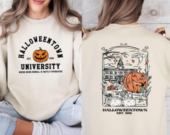 May include: A cream-colored sweatshirt featuring a front graphic with an orange jack-o'-lantern and the text HALLOWEENTOWN UNIVERSITY EST. 1998 WHERE BEING NORMAL IS VASTLY OVERRATED. The back displays a detailed illustration of a building and pumpkin.