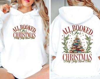 May include: White hoodie with the text "ALL BOOKED for CHRISTMAS Holly Jolly Book Club" in red and green. The back of the hoodie features a Christmas tree made of books, surrounded by green leaves and stars.