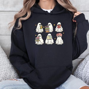 May include: Black hooded sweatshirt with a playful design of cartoon ghosts reading books. Each white ghost has a simple face and is holding or wearing books. Yellow stars are scattered around the ghosts.
