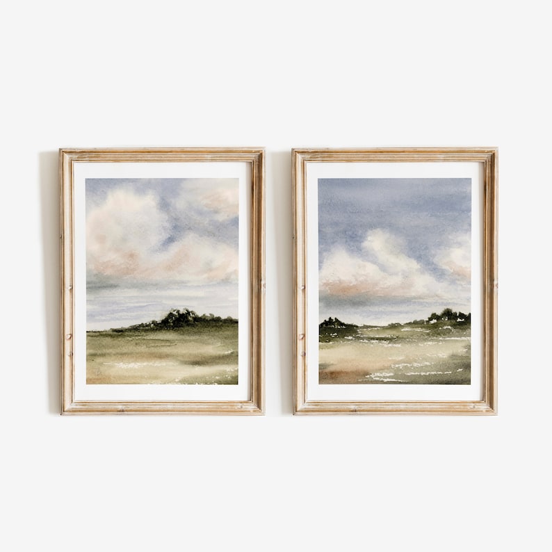 May include: Two framed watercolour paintings of a landscape with a field, trees, and a cloudy sky. The paintings are in a light wood frame.