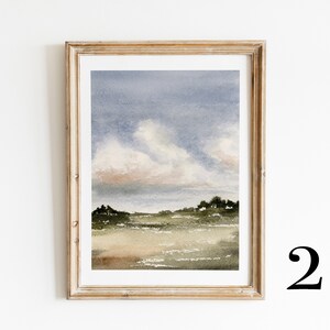 May include: A framed watercolour painting of a landscape with a field, trees, and a cloudy sky. The sky is a soft blue with pink and white clouds. The field is a light green with brown and green trees in the distance.