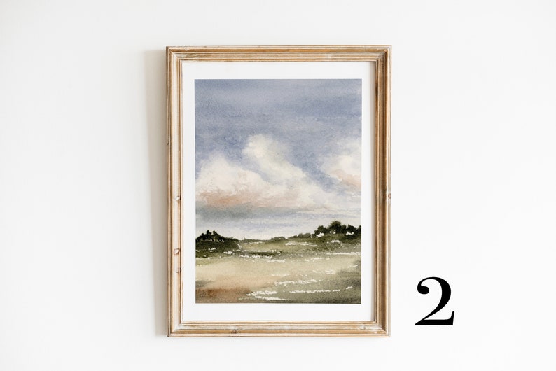 May include: A framed watercolour painting of a landscape with a field, trees, and a cloudy sky. The sky is a soft blue with pink and white clouds. The field is a light green with brown and green trees in the distance.