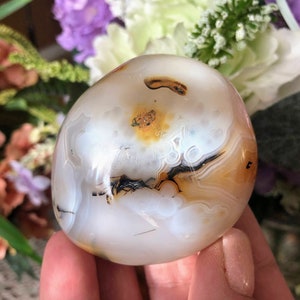 May include: A white agate sphere with brown and black banding. The sphere has a smooth, polished surface and is a natural stone.