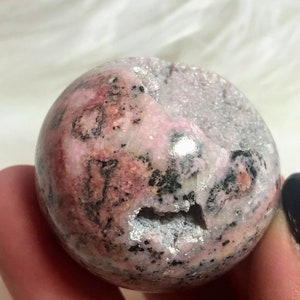 May include: A pink and grey sphere with black and white markings. The sphere is made of polished stone and has a rough, natural texture.