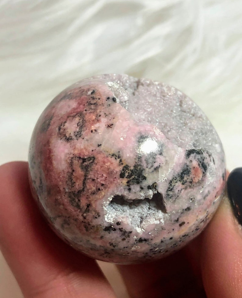 May include: A pink and grey sphere with black and white markings. The sphere is made of polished stone and has a rough, natural texture.