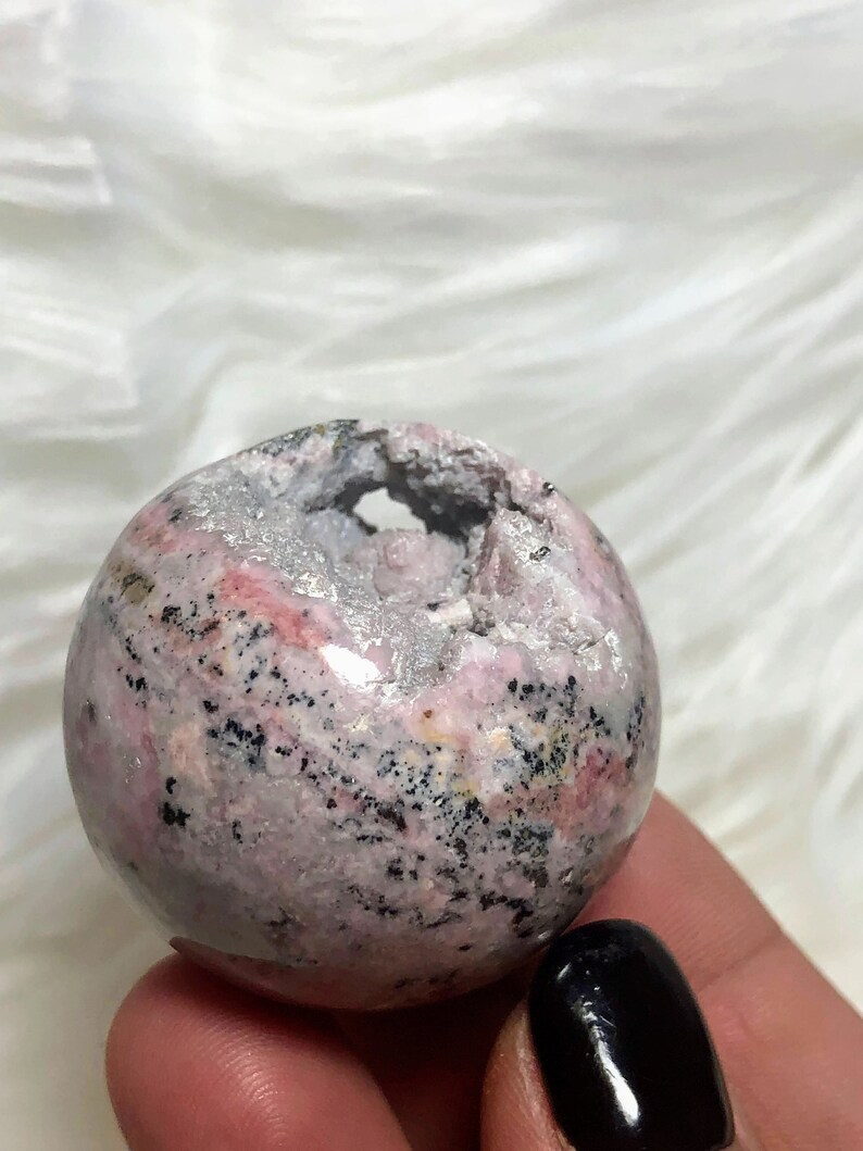 May include: A pink and grey sphere with black flecks and a hole in the centre. The sphere is made of natural stone.