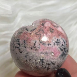 May include: A pink and grey sphere with black and white markings. The sphere is made of polished stone and has a smooth, rounded surface.