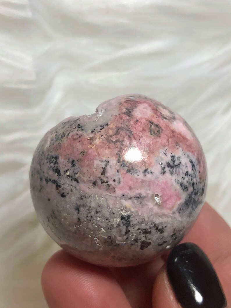 May include: A pink and grey sphere with black and white markings. The sphere is made of polished stone and has a smooth, rounded surface.