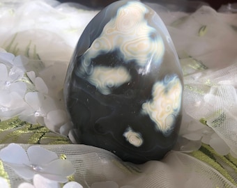 May include: A smooth, gray and white agate stone with a unique, swirling pattern. The stone is shaped like an egg and has a polished finish.