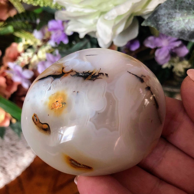 May include: White agate sphere with brown and black dendritic patterns and yellow inclusions. The sphere is smooth and polished.