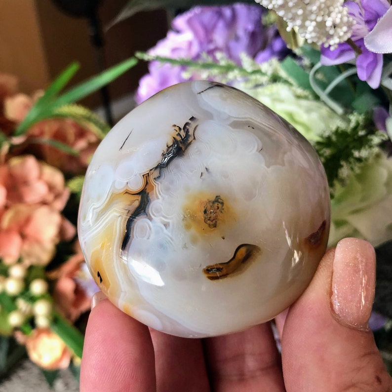 May include: A white agate sphere with brown and black banding. The sphere is smooth and polished.