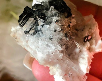May include: A cluster of clear quartz crystals with a black, metallic mineral embedded in the center.