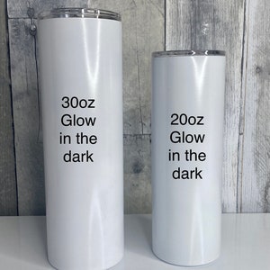 May include: Two white stainless steel tumblers with black text. The larger tumbler says "30oz Glow in the dark" and the smaller tumbler says "20oz Glow in the dark".