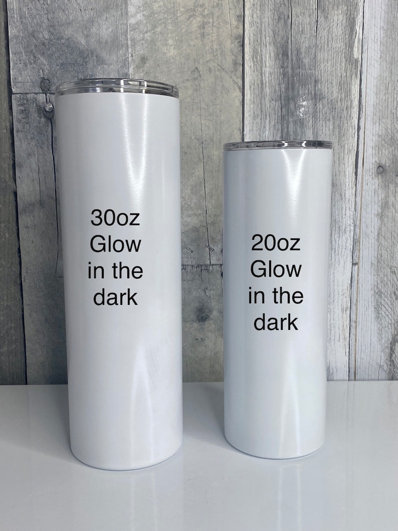May include: Two white stainless steel tumblers with black text. The larger tumbler says "30oz Glow in the dark" and the smaller tumbler says "20oz Glow in the dark".