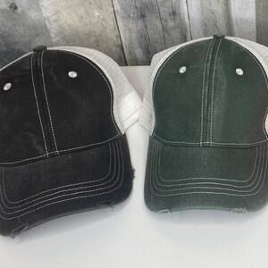 K&ouml;nnte beinhalten: Zwei abgenutzte Trucker-Caps mit wei&szlig;en Mesh-R&uuml;ckenteilen. Eine M&uuml;tze ist schwarz mit wei&szlig;en N&auml;hten und die andere ist dunkelgr&uuml;n mit wei&szlig;en N&auml;hten.