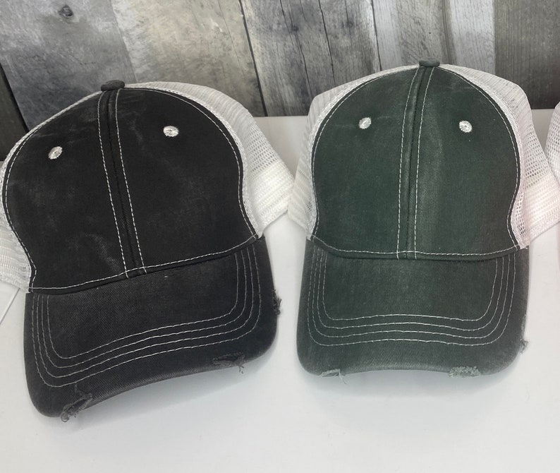 K&ouml;nnte beinhalten: Zwei abgenutzte Trucker-Caps mit wei&szlig;en Mesh-R&uuml;ckenteilen. Eine M&uuml;tze ist schwarz mit wei&szlig;en N&auml;hten und die andere ist dunkelgr&uuml;n mit wei&szlig;en N&auml;hten.