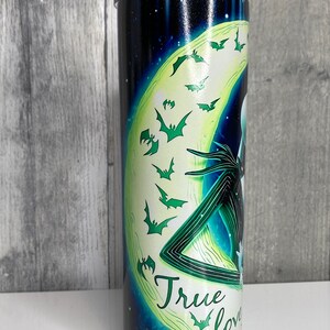 May include: A black and green stainless steel tumbler with a graphic of Jack Skellington and Sally from the Nightmare Before Christmas movie. The graphic features a crescent moon with bats flying around it. The text "True Love" is written on the tumbler.