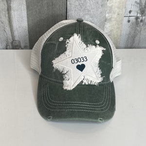 May include: A green and white trucker hat with a distressed white star patch and the number "03033" with a black heart in the center.