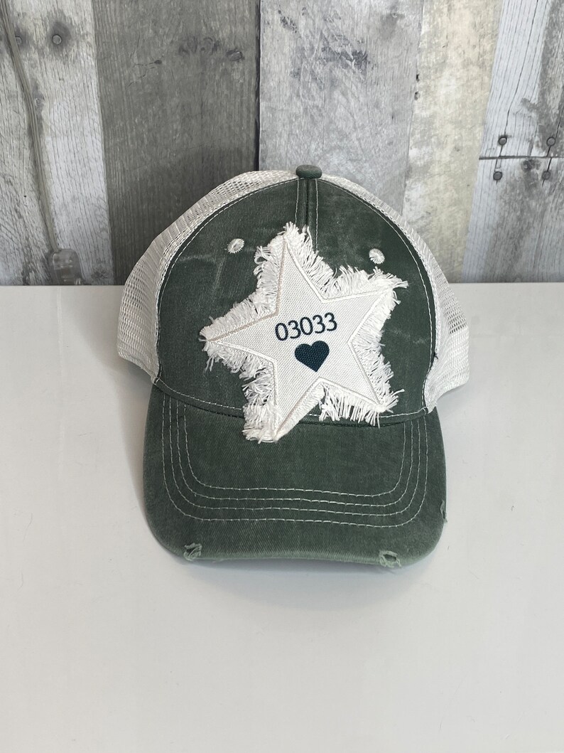 K&ouml;nnte beinhalten: Eine gr&uuml;ne und wei&szlig;e Trucker-Kappe mit einem abgenutzten wei&szlig;en Stern-Patch und der Nummer "03033" mit einem schwarzen Herzen in der Mitte.