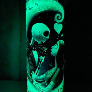 May include: A glow-in-the-dark tumbler with a black and white illustration of Jack Skellington and Sally from The Nightmare Before Christmas. The text "Our Love Never Dies" is written on the tumbler.
