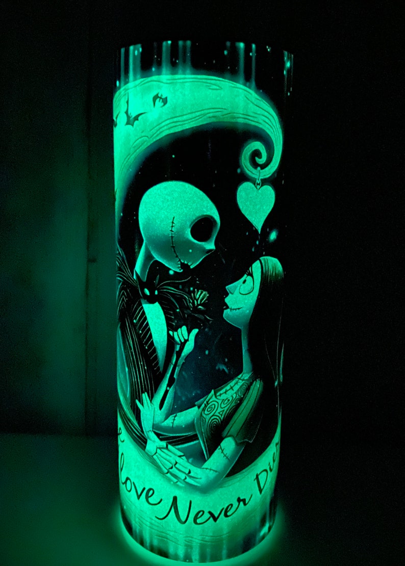 May include: A glow-in-the-dark tumbler with a black and white illustration of Jack Skellington and Sally from The Nightmare Before Christmas. The text "Our Love Never Dies" is written on the tumbler.
