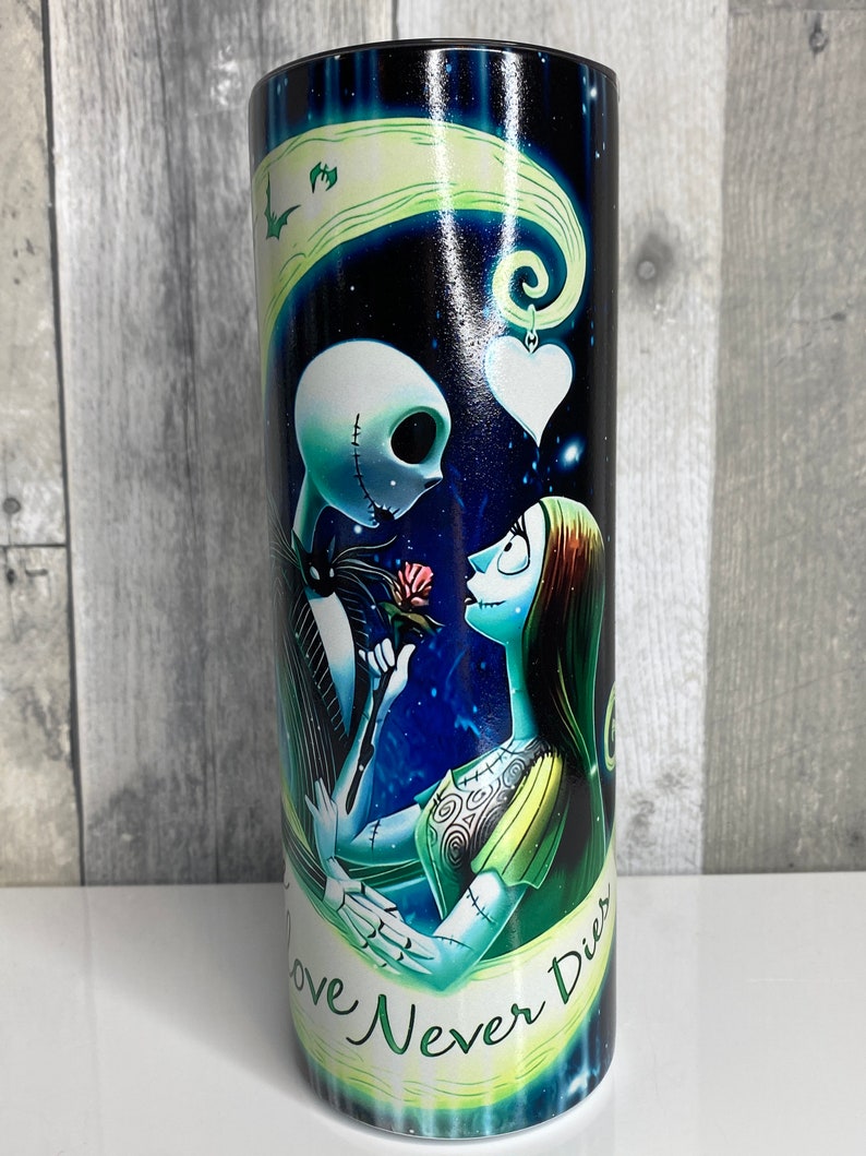 May include: A black and blue stainless steel tumbler with a graphic of Jack Skellington and Sally from the Nightmare Before Christmas movie. The graphic shows them holding a rose and the text "Love Never Dies".