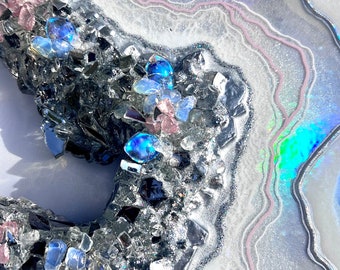May include: A white and silver resin art piece with a geode design. The geode is filled with iridescent glitter and small blue and pink glass pieces.