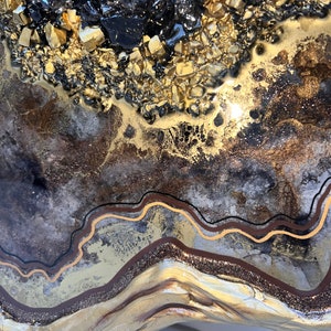 Op de afbeelding: Abstracte harskunst met een gouden en zwarte kleurstelling. Het hars is gelaagd en getextureerd, met een gouden glitterafwerking. De kunst is in de vorm van een hart.