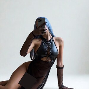 May include: A black halter dress with a lace-up bodice and a sheer skirt. The dress is paired with sheer gloves. The model has blue hair and is holding a phone.
