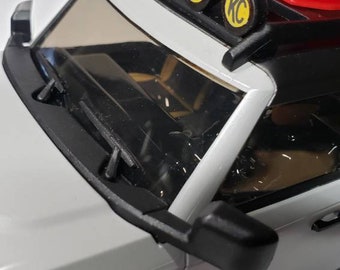 May include: A white toy truck with black accents and a black roof rack. The truck has four yellow KC lights on the roof rack. The truck is sitting on a white surface.