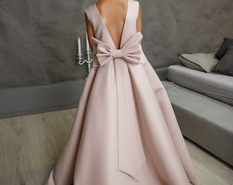 May include: A pale pink satin dress with a large bow on the back. The dress has a low back and a full skirt.