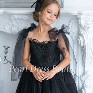 Puede incluir: Una ni&ntilde;a peque&ntilde;a con un vestido de tul negro con un corpi&ntilde;o de encaje y lazos de tul negro en los hombros. El vestido tiene una falda completa y es perfecto para una ocasi&oacute;n especial.