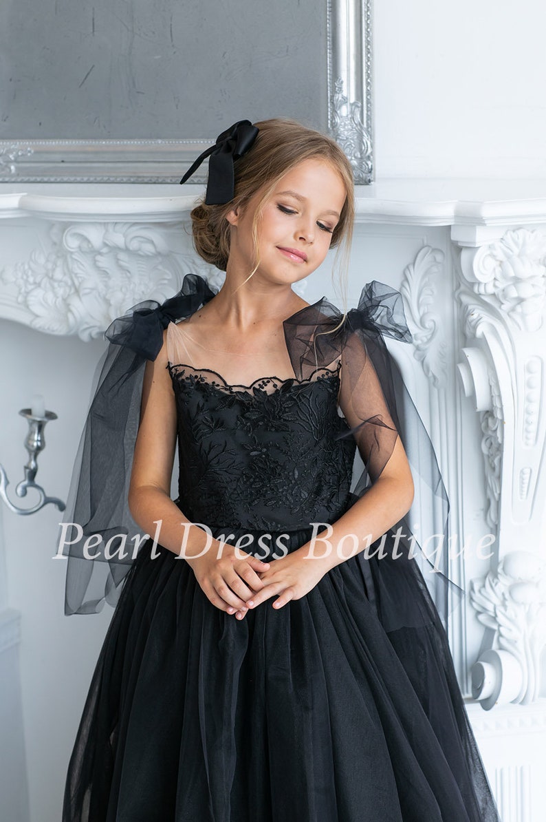 Puede incluir: Una ni&ntilde;a peque&ntilde;a con un vestido de tul negro con un corpi&ntilde;o de encaje y lazos de tul negro en los hombros. El vestido tiene una falda completa y es perfecto para una ocasi&oacute;n especial.