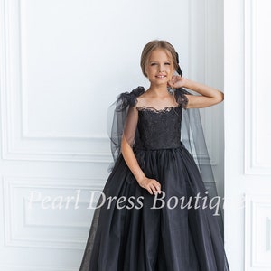 Puede incluir: Una ni&ntilde;a peque&ntilde;a con un vestido de tul negro con un corpi&ntilde;o de encaje y una capa de tul. El vestido tiene un escote de coraz&oacute;n y est&aacute; adornado con delicados bordados. La ni&ntilde;a sonr&iacute;e y mira a la c&aacute;mara. El vestido es perfecto para una ocasi&oacute;n especial.