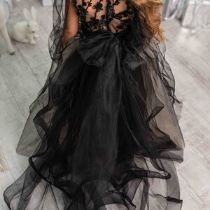 May include: A black tulle dress with a sheer bodice and floral embroidery. The dress has a large bow at the waist and a long train.
