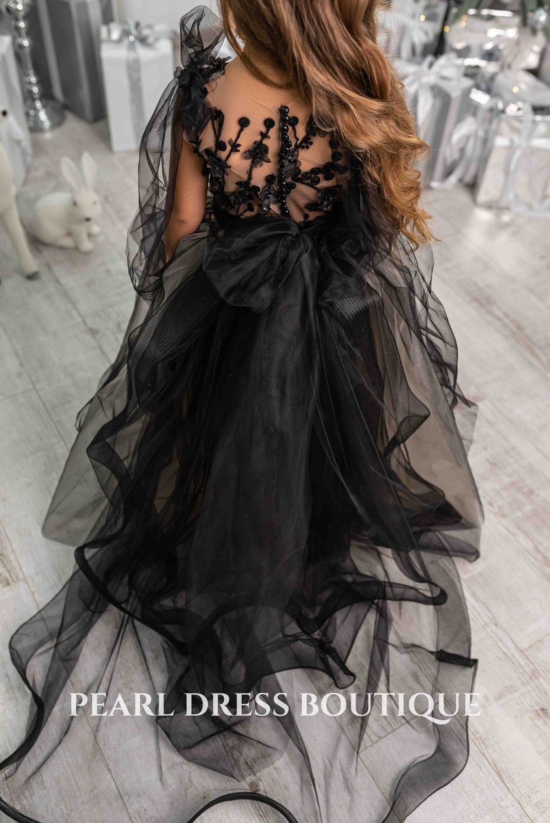 May include: A black tulle dress with a sheer bodice and floral embroidery. The dress has a large bow at the waist and a long train.
