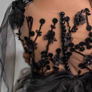 May include: Black tulle dress with floral embroidery and pearl beading. The dress has a sheer back with a row of black buttons. The dress is labeled "PEARL DRESS BOUTIQUE".