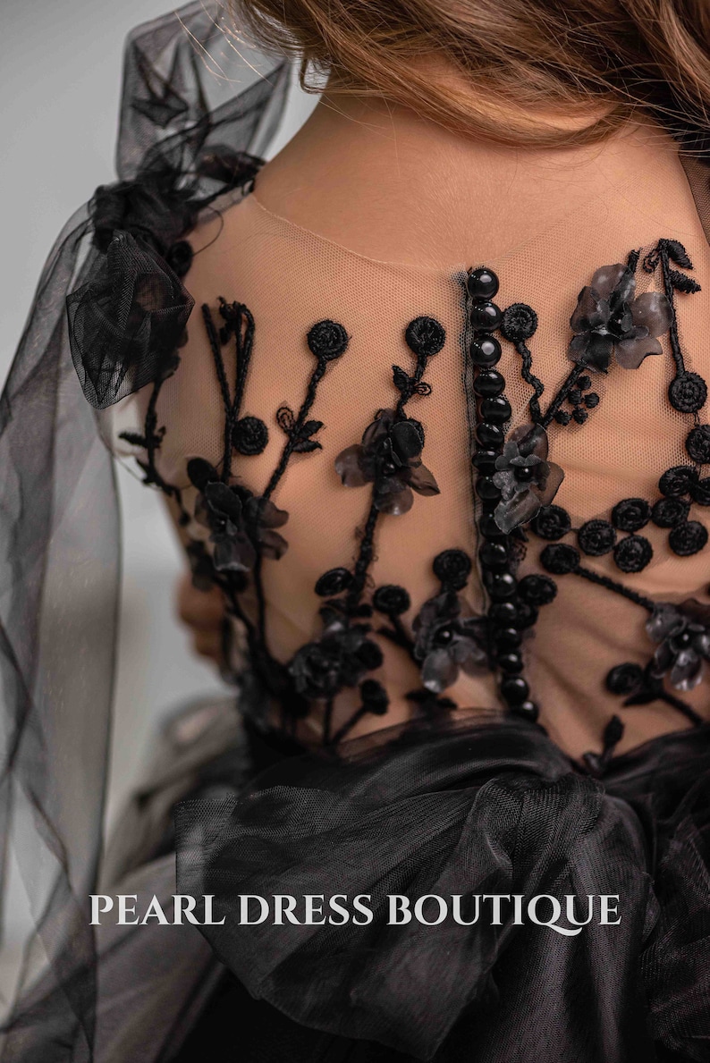 May include: Black tulle dress with floral embroidery and pearl beading. The dress has a sheer back with a row of black buttons. The dress is labeled "PEARL DRESS BOUTIQUE".
