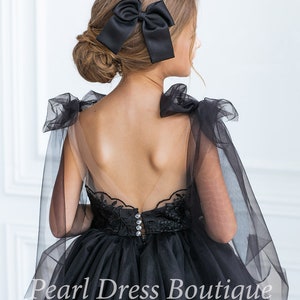 Puede incluir: Un vestido de tul negro con un corpi&ntilde;o de encaje y una espalda transparente. El vestido tiene un lazo en la espalda y una superposici&oacute;n de tul. El vestido es para una ni&ntilde;a y es perfecto para una ocasi&oacute;n especial.